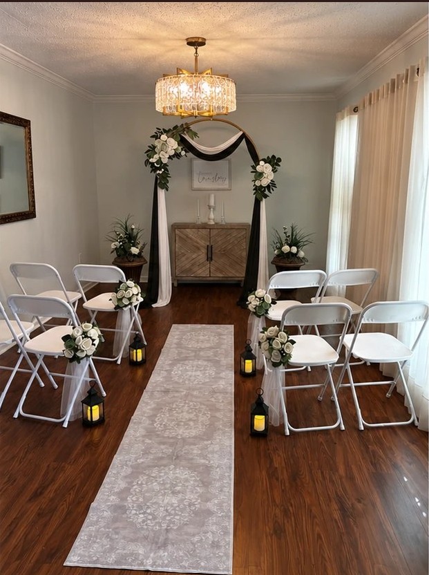 The ceremony room styled in black and white, with a black and ivory draped arch, white flowers, and lanterns along the aisle